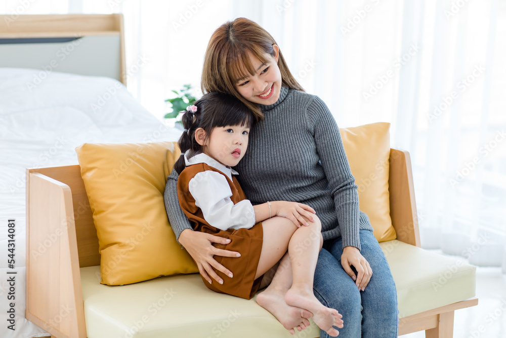 Millennial Asian cheerful happy young pretty female teenager mother nanny babysitter in casual outfit sitting on cozy sofa smiling hugging showing love with little cute preschooler daughter girl Millennial Asian cheerful happy young pretty female teenager mother nanny babysitter in casual outfit sitting on cozy sofa smiling hugging showing love with little cute preschooler daughter girl