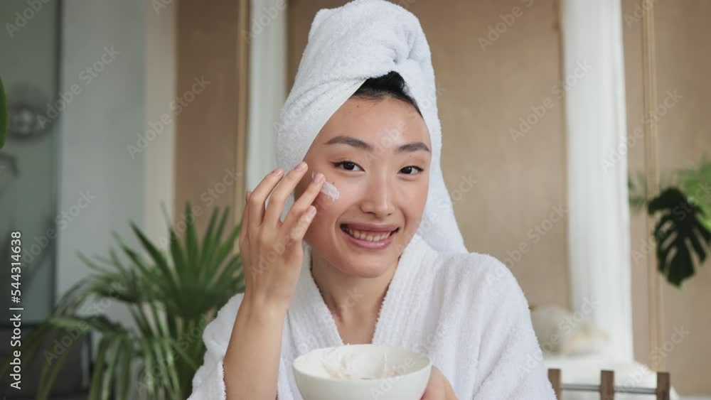 Happy asian woman holding bowl applying white mask homemade moisturizing and nourishing face mask or cream making mixture with natural cosmetic products. Happy asian woman holding bowl applying white mask homemade moisturizing and nourishing face mask or cream making mixture with natural cosmetic products.