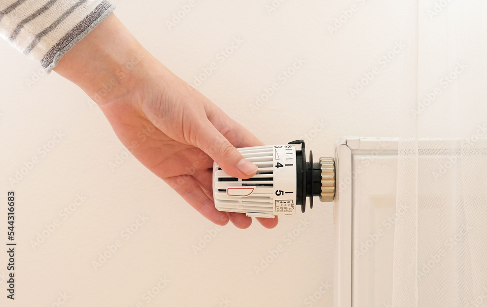 Woman regulates temperature at home with the heating thermostat to save energy, closeup with