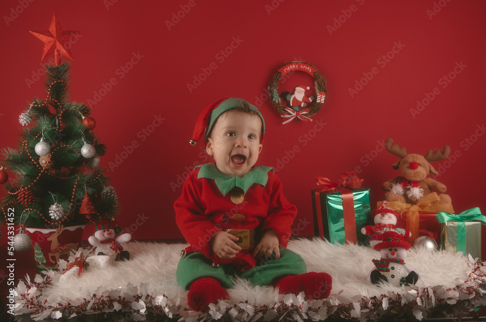 Nice boy dressed as an elf next to Christmas decorations with a tree and gifts Nice boy dressed as an elf next to Christmas decorations with a tree and gifts
