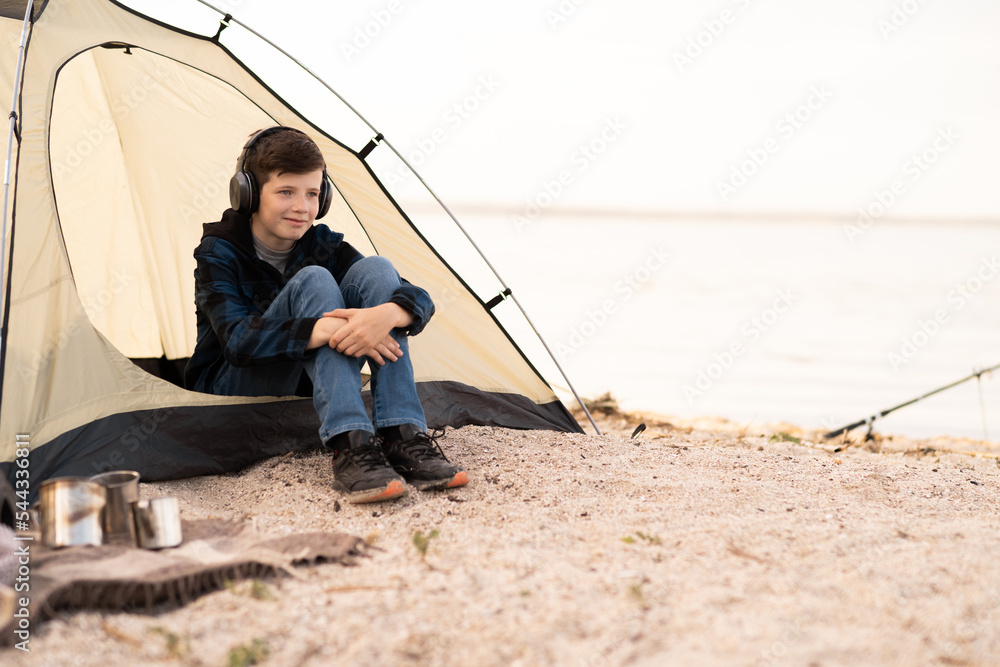 Young boy on camping trip.Child in a tent on beach listening music. Camping. Happy teen at spring vacations.