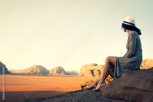 Cute young dreamy woman traveler barefoot sit viewpoint enjoy calm morning in Wadi rum desert in Jordan.Vintage travel carefree holiday tourism concept
