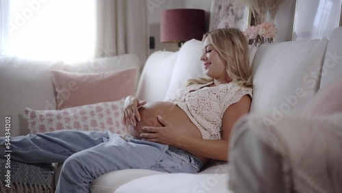 Tender image of Happy caucasian pregnant mom caressing belly near window indoors. Beautiful mother lying on the sofa. Advanced stage of gestation woman rest at home. Concept of family and motherhood.  photo