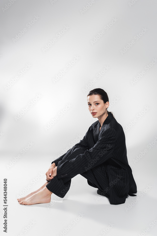 Young barefoot model in striped suit looking at camera while sitting on grey background. Young barefoot model in striped suit looking at camera while sitting on grey background.