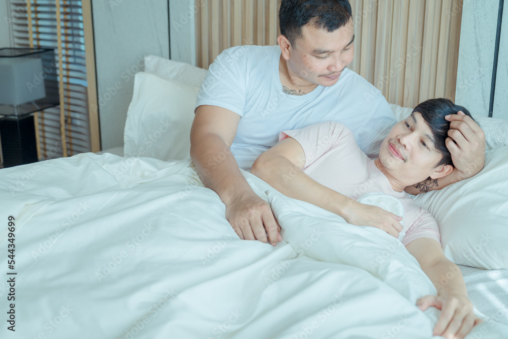 Asian young male gay family lying down on bed and look at each other. Attractive handsome LGBTQ couple in pajamas, feel happy after wake up in morning and kiss forehead of boyfriend in bedroom at home Asian young male gay family lying down on bed and look at each other. Attractive handsome LGBTQ couple in pajamas, feel happy after wake up in morning and kiss forehead of boyfriend in bedroom at home