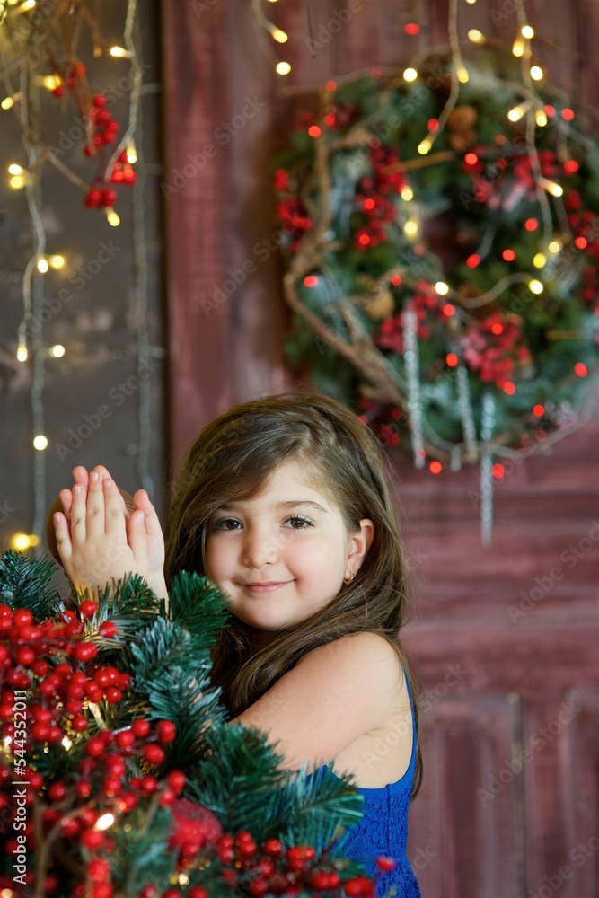 Baby girl in festive attire is in the room decorated for the new year and Christmas.