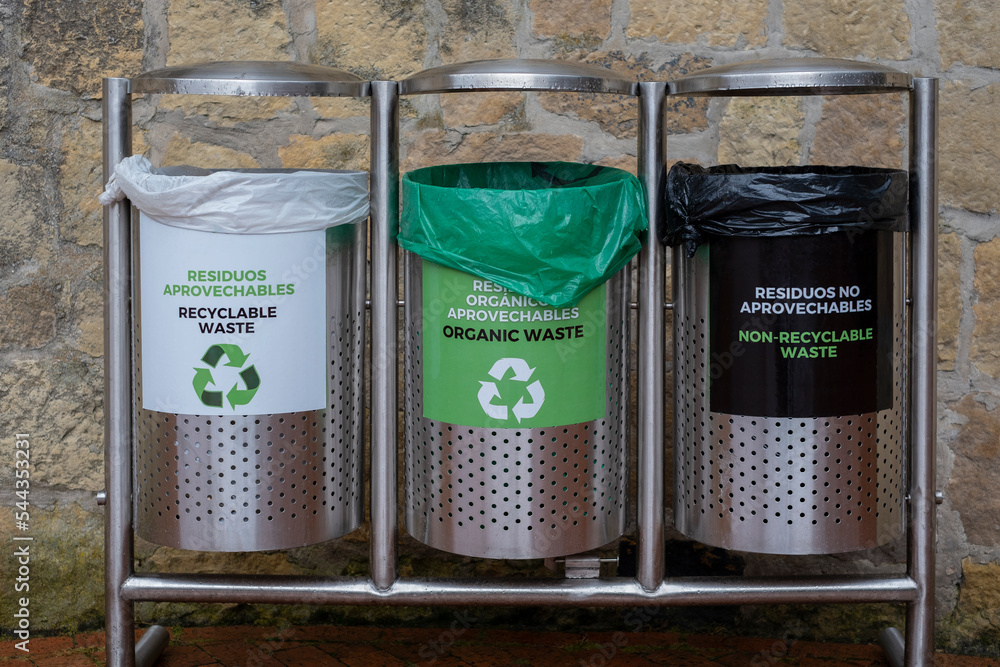 Three garbage trash bins with signs in Spanish and English recyclable