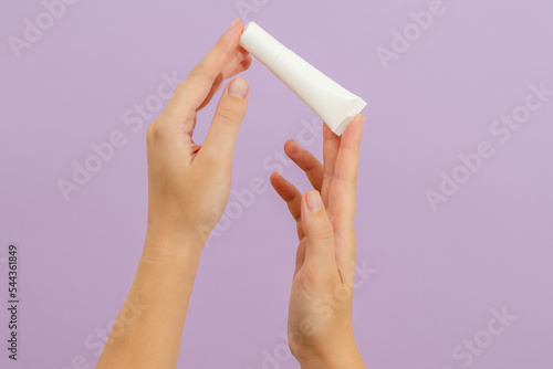 Hand holds plastic white tube isolated on lilac background. Beauty concept. Packaging tube for cosmetic products
