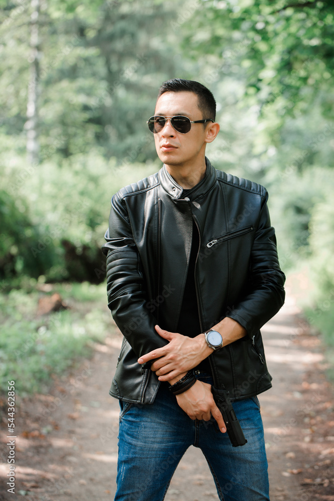 A man in a black leather jacket holds a gun in his hands A man in a black leather jacket holds a gun in his hands
