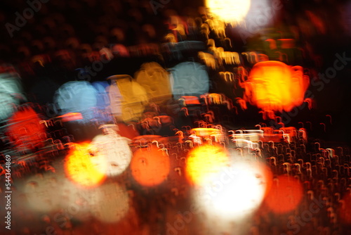 Colorful bokeh of vehicle headlights on glass on rainy day at night.