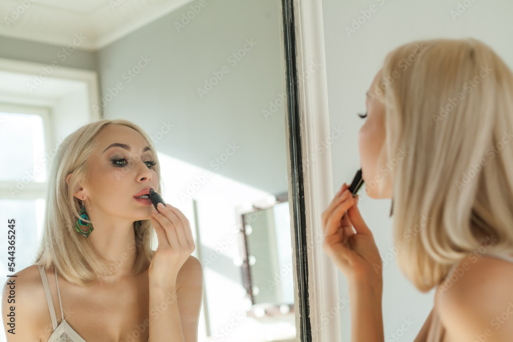 Beautiful blonde woman is applying lipsick make up and looking to the mirror Beautiful blonde woman is applying lipsick make up and looking to the mirror