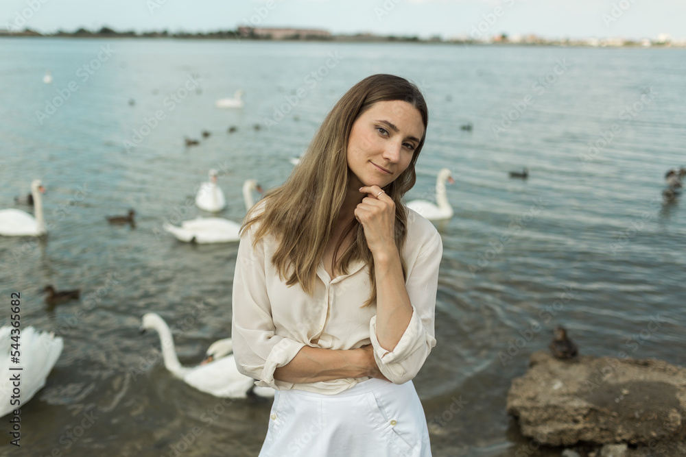 young woman stands next to a beautiful lake and white swans