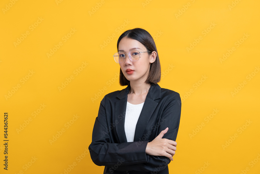 Portrait of beautiful asian business woman wearing glasses and black suit, she folded arms on yellow isolate background she look so smart and serious. Portrait of beautiful asian business woman wearing glasses and black suit, she folded arms on yellow isolate background she look so smart and serious.