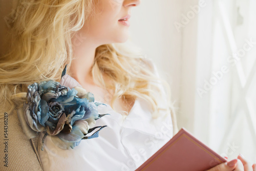Print op canvas A woman with a large brooch is reading a book by the window