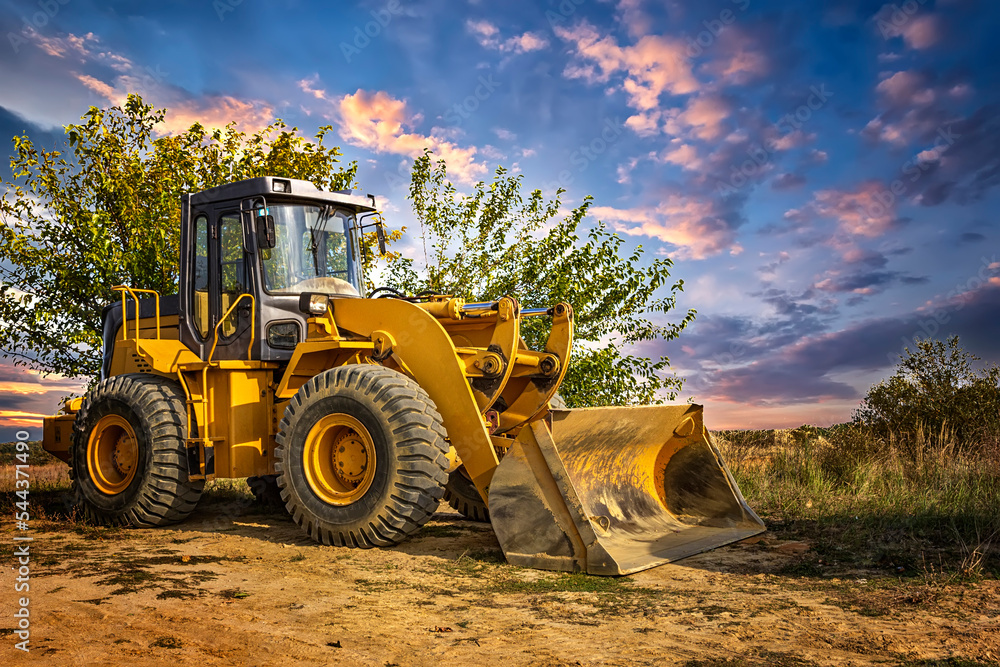 A bulldozer or loader moves the earth at the construction site against the sunset sky A bulldozer or loader moves the earth at the construction site against the sunset sky