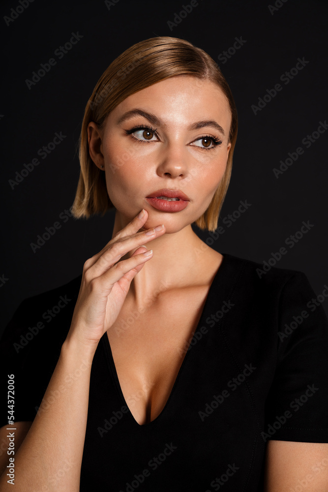 Young beautiful woman touching her chin and looking aside isolated over black background Young beautiful woman touching her chin and looking aside isolated over black background