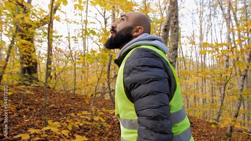 Amber alert. Middle aged man volunteer wearing bright green vest searching for missed person in wild autumn forest, walking in woodland and shouting.