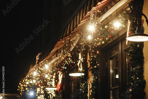 Stylish christmas illumination and festive lights on fir branches in evening outdoor. Modern christmas decor in city street. Atmospheric winter holidays in Europe. Merry Christmas!