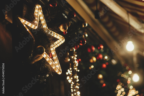 Merry Christmas! Stylish christmas star illumination and festive lights on fir branches in evening outdoor. Modern christmas decor in city street. Atmospheric winter holidays in Europe.