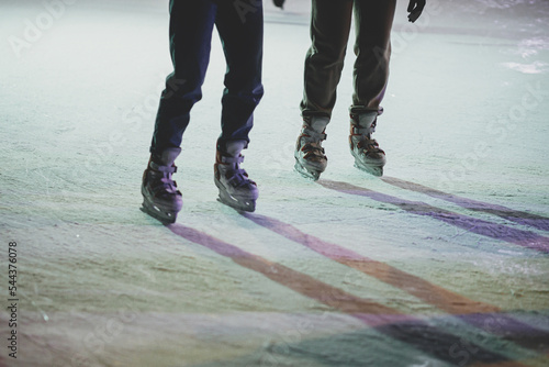 Ice skaters on ice rink, skates close up. People having fun and skating in town square in evening.Legs with ice skaters cropped view. Atmospheric Winter holidays in Europe. Happy Holidays! photo