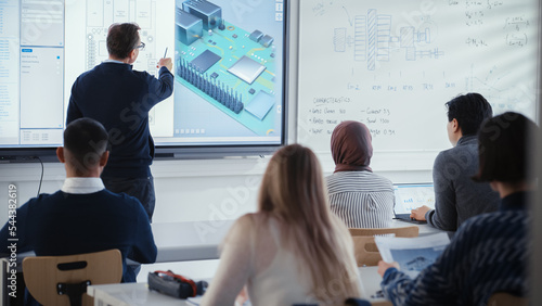Male Teacher Stands Next to Digital Interactive Whiteboard and Points at Processor During Lesson About Computer Motherboard Components with Group of Diverse Engineering Students.