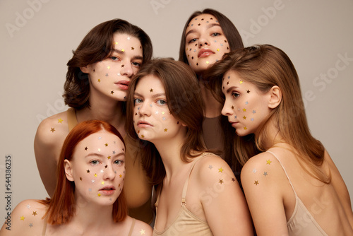 Portrait of five young beautiful women posing together in beige underwear isolated over grey background. Starry makeup