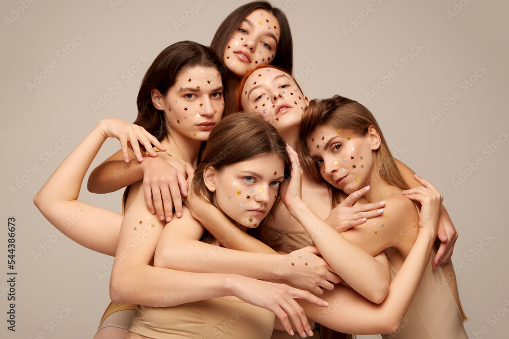Fototapeta premium Portrait of young beautiful women with smooth skin posing in beige underwear isolated over grey background. Hugs