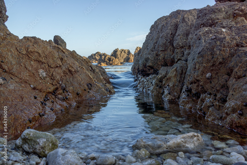 tide coming in through boulders at the sea. blue and brown