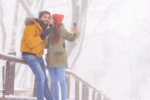 Couple taking selfies and drinking hot tea outdoors while on winter vacation