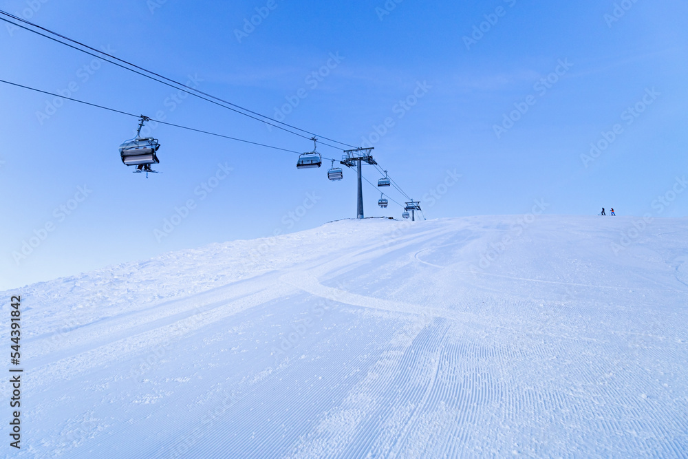 Ski chair lift on top of mountain, ski slope prepared for skiing, minimal style blue monochrome winter in Sheregesh ski resort. White snow, clear sky, cable road and small people on peak Ski chair lift on top of mountain, ski slope prepared for skiing, minimal style blue monochrome winter in Sheregesh ski resort. White snow, clear sky, cable road and small people on peak