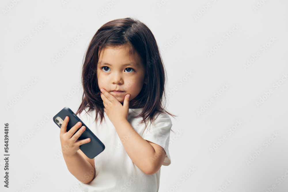 pensive girl of preschool age stands on a light background with a phone pensive girl of preschool age stands on a light background with a phone