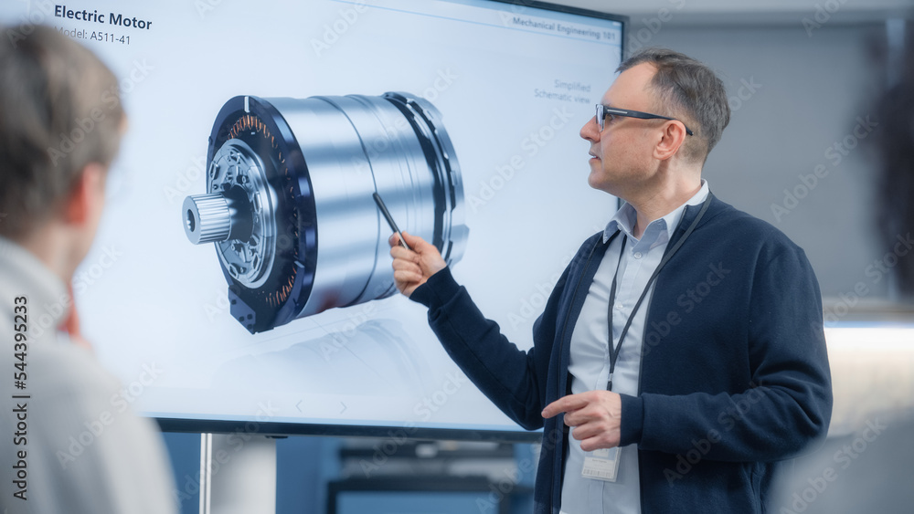 Fototapeta premium Male Chief Engineer Talks to Young Specialists About Components of the Electric Motor and Using Big Screen. Engineering and Green Electric Energy Innovative Technologies Concept.