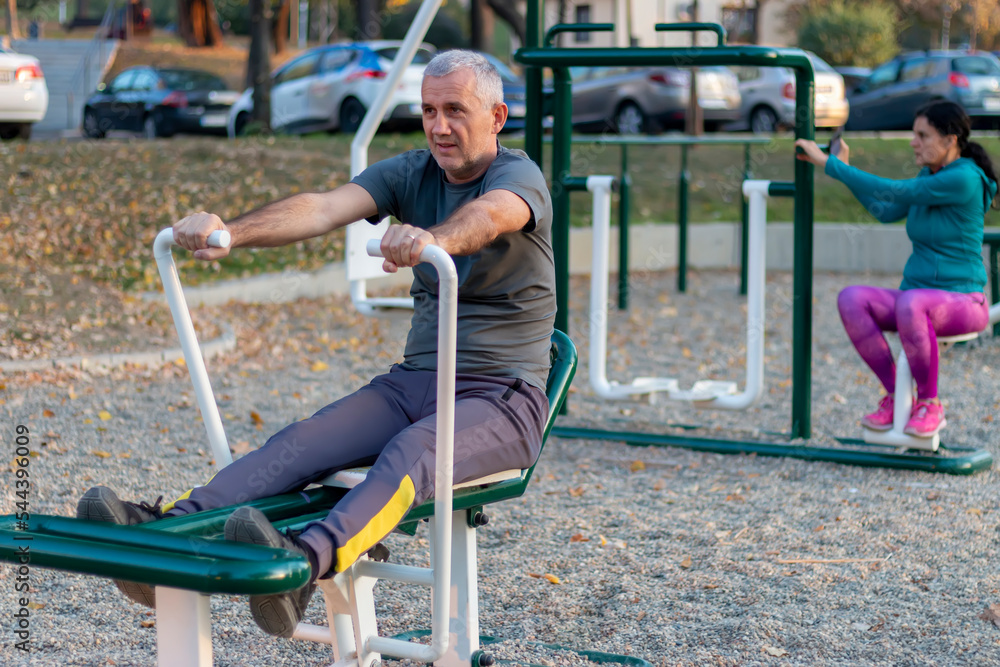 Fototapeta premium Mature man working out in the gym and leading a healthy and active lifestyle. Outdoor sports area with equipment, facilities for working out, stretching, cardio and strength physical activity.
