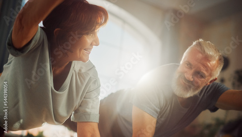 Middle Aged Couple Doing Core Strengthening Exercises Together at Home in Sunny Living Room. Senior Man and Woman Motivate Each Other to be Healty. Lifestyle and Fitness Concept. © Gorodenkoff