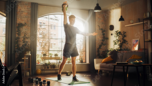 Fotografie, Obraz Strong Athletic Fit Young Man Lifting a Heavy Kettlebell, Doing Core Strengthening Exercises During Morning Workout at Home in Bright Apartment