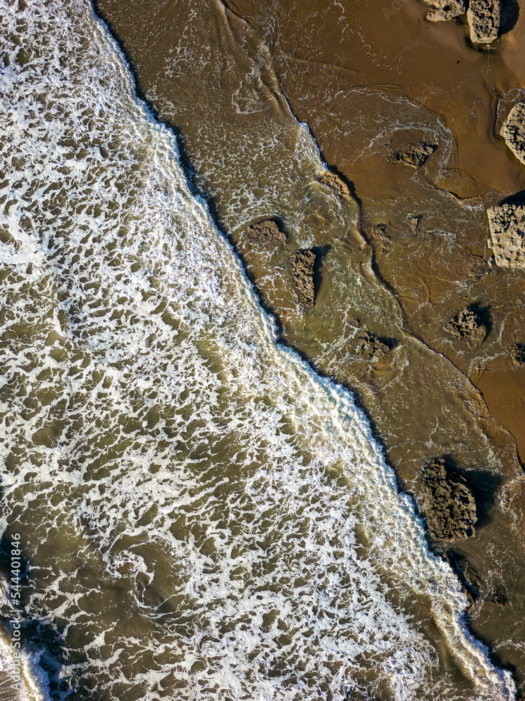 Top down areial view of waves breaking against rocks and a sandy beach Top down areial view of waves breaking against rocks and a sandy beach