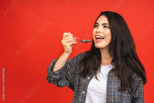 Time for dinner! Portrait of young beautiful woman wearing red casual shirt, holding spoon isolated over red background.