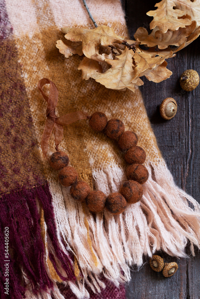 Woolen scarf, beads, dry oak branch and acorns on a wooden background.