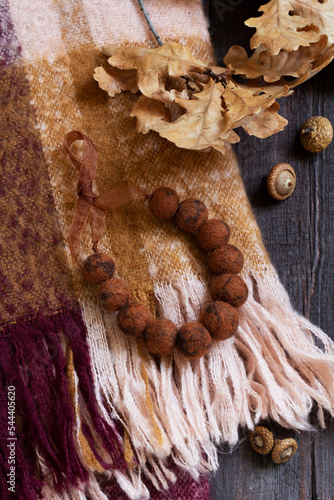Obraz na płótnie Woolen scarf, beads, dry oak branch and acorns on a wooden background. w salonie