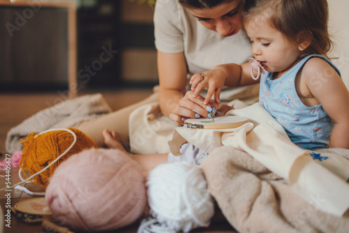 Billede på lærred The caring mother teaching her child to embroider from an early age sitting on the floor