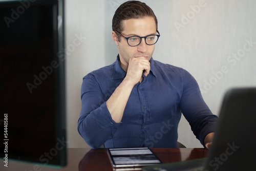 Businessman works from remote at house with a laptop due to coronavirus quarantine. Handsome Italian guy in glasses at the computer working away in smartworking photo