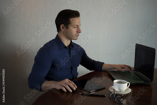 Businessman works from remote at house with a laptop due to coronavirus quarantine. Handsome Italian guy in glasses at the computer working away in smartworking photo