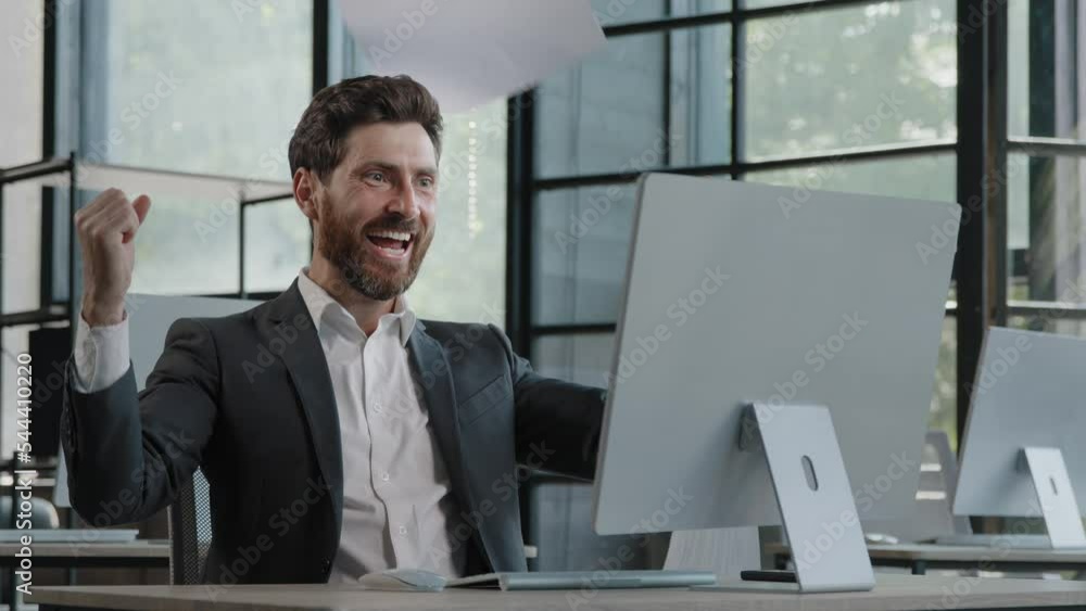 Caucasian 40s bearded boss investor entrepreneur employer man in office with computer looks at papers reads good news financial growth of business throws documents into air rejoices in winning triumph