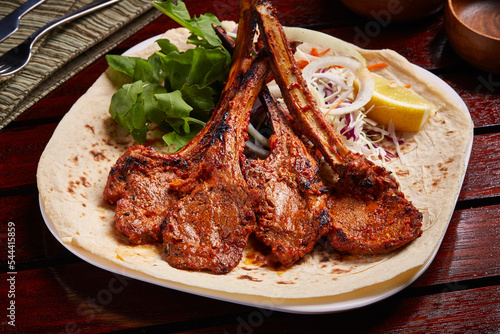 Grilled Lamb Chops with lemon, salad and bread served in dish isolated on table side view of middle east food photo