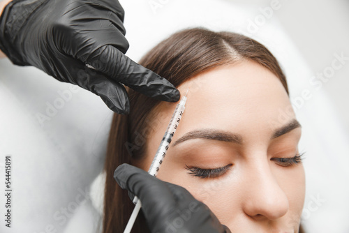 A cosmetologist makes anti-aging injections against wrinkles on the forehead on the face of a beautiful woman. Women's aesthetic cosmetology in a beauty salon.