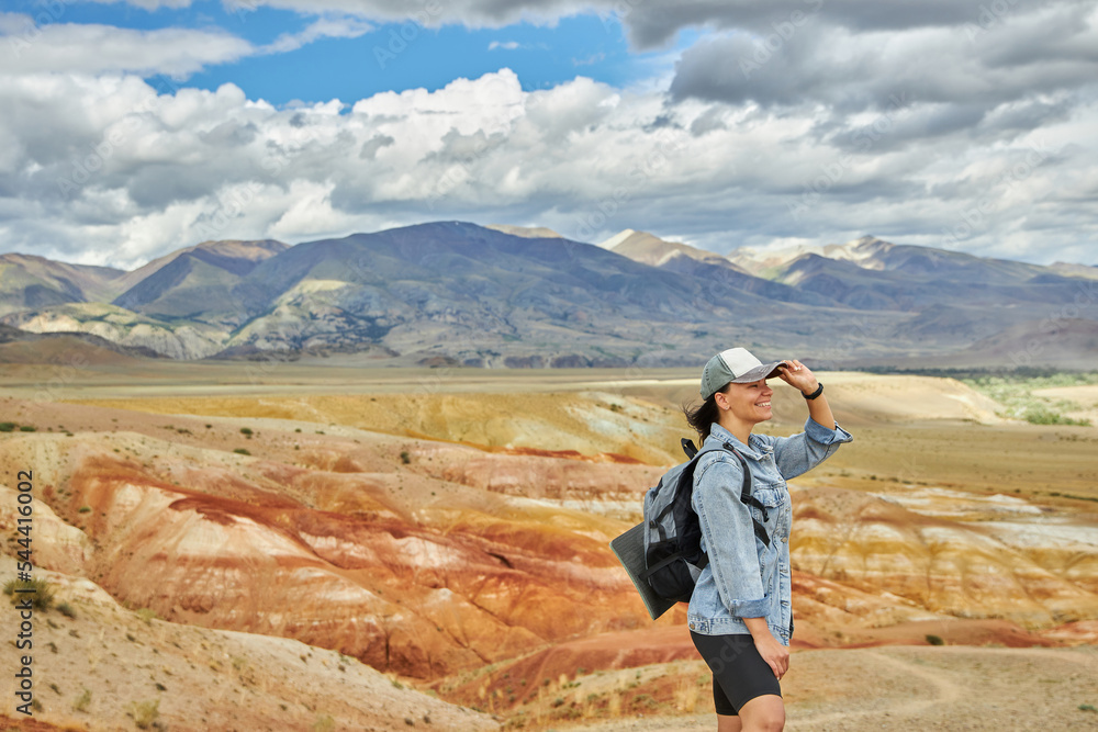 woman tourist in jeans jacket stands against backdrop of sandy hilly landscape. Sights of Russia, Siberia and Altai Republic, mars field. Tourism, travel and adventure. Kosh-agach, Chagan-Uzun