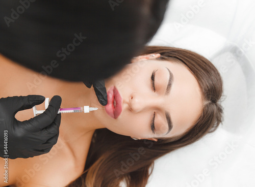 female lips, lip augmentation procedure. A syringe near a woman's mouth, injections to increase the shape of the lips