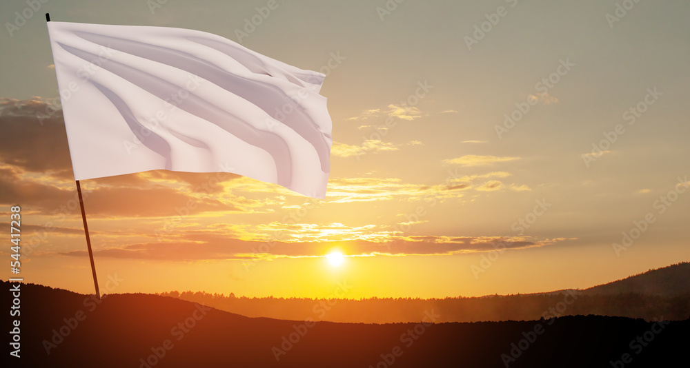 White flag waving in the wind on flagpole against the sunset sky with ...