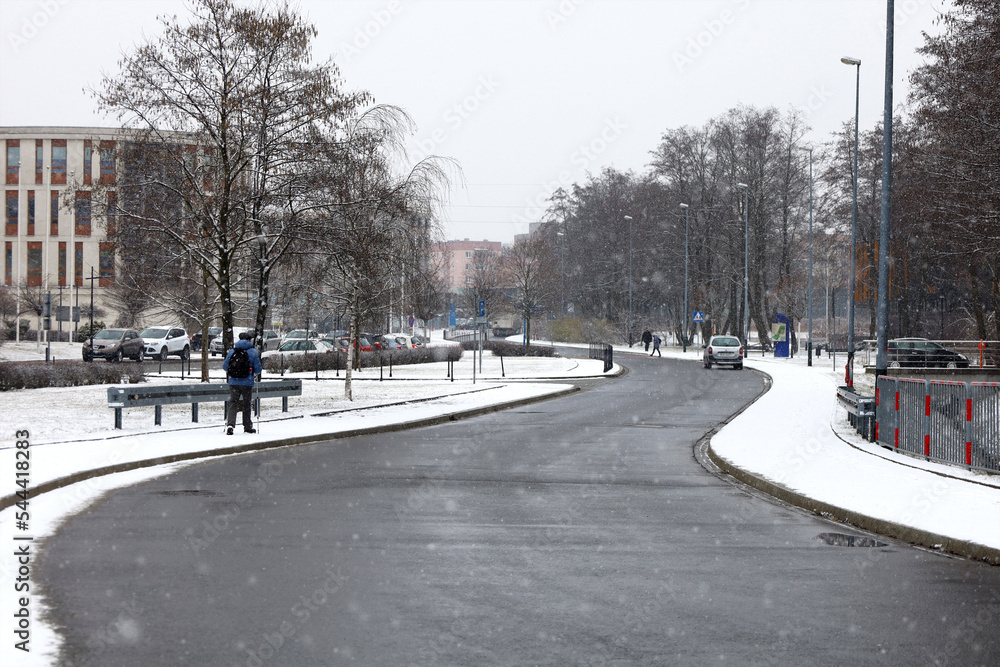 Empty road in winter on background, beginning of snowfall, snowflakes defocused and blurred in foreground. Pedestrian on sidewalk, cars in the distance, not recognizable.