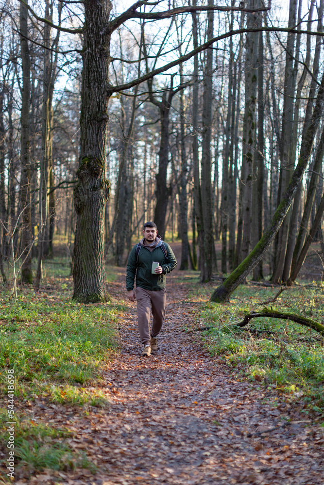 Obraz premium A man walks a dog in an autumn forest park, plays with a stick, drinks coffee in a reusable thermocup